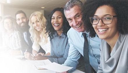 A culturally diverse group of business people happily smiling around a desk.