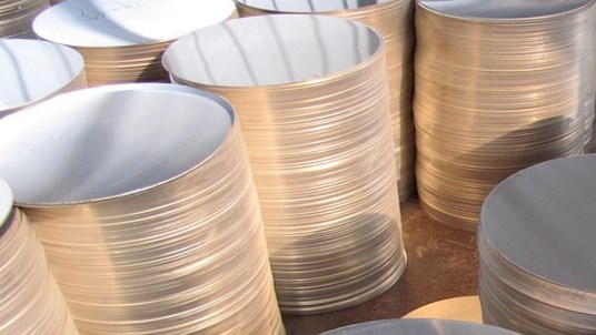 Multiple tall stacks of shiny round aluminum discs, prepared for industrial manufacturing and processing.
