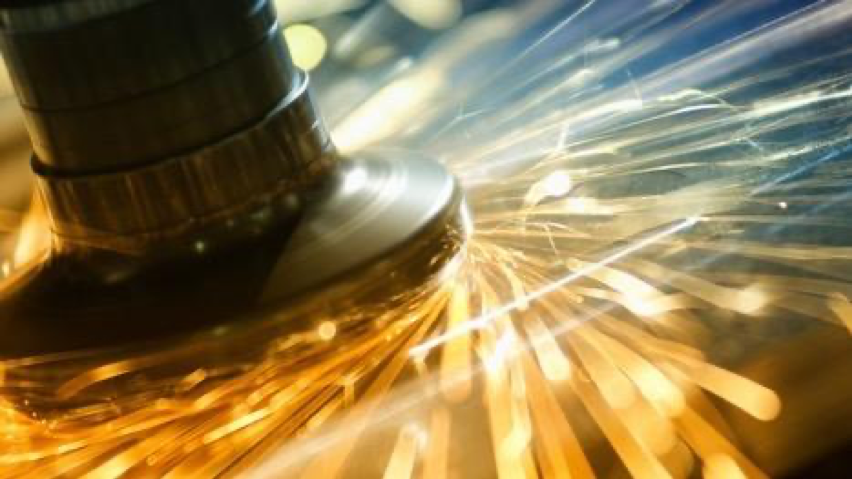 Metal processing machinery with orange sparks flying off in a spiral-like motion