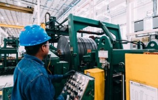 National Material Company’s partner company, National Material of Mexico’s brightly lit steel processing facility. A steel-processing equipment operator wearing all blue protective gear and clothing carefully monitors his machinery.