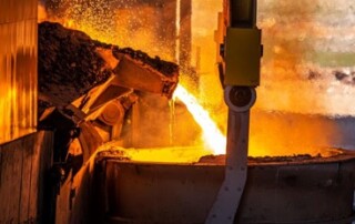 Red-hot molten steel pours into a vat, emitting bright orange light, fumes, and sparks.