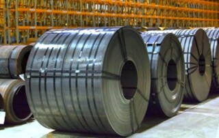 A photograph of a row of large steel coils neatly banded at National Material Company’s brightly lit steel processing plant and warehouse in Riverdale, Illinois.