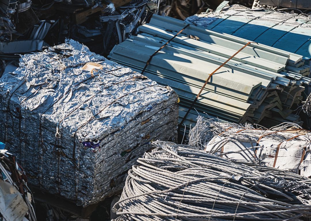 nmc-2025-12-blog-in-text-img1-metal-scraps Bales of compressed aluminum scrap, bundled cables, and stacked metal sheets are sorted for recycling. This collection of raw feedstock is prepared for handling by a metal processing company.