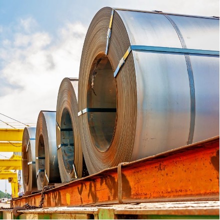 NMC-2026-07-steel-coil-inventory Steel coils loaded on a flatbed delivery truck, illustrating just-in-time logistics for OEM metal supply chain sourcing.