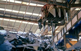 Industrial crane sorting through metal scrap, representing the results of poor metal processing that lead to increased production costs for OEMs.
