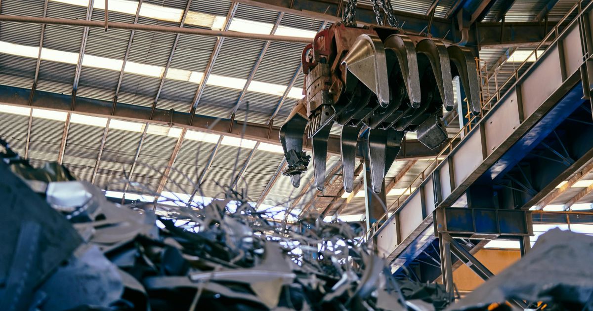 Industrial crane sorting through metal scrap, representing the results of poor metal processing that lead to increased production costs for OEMs.